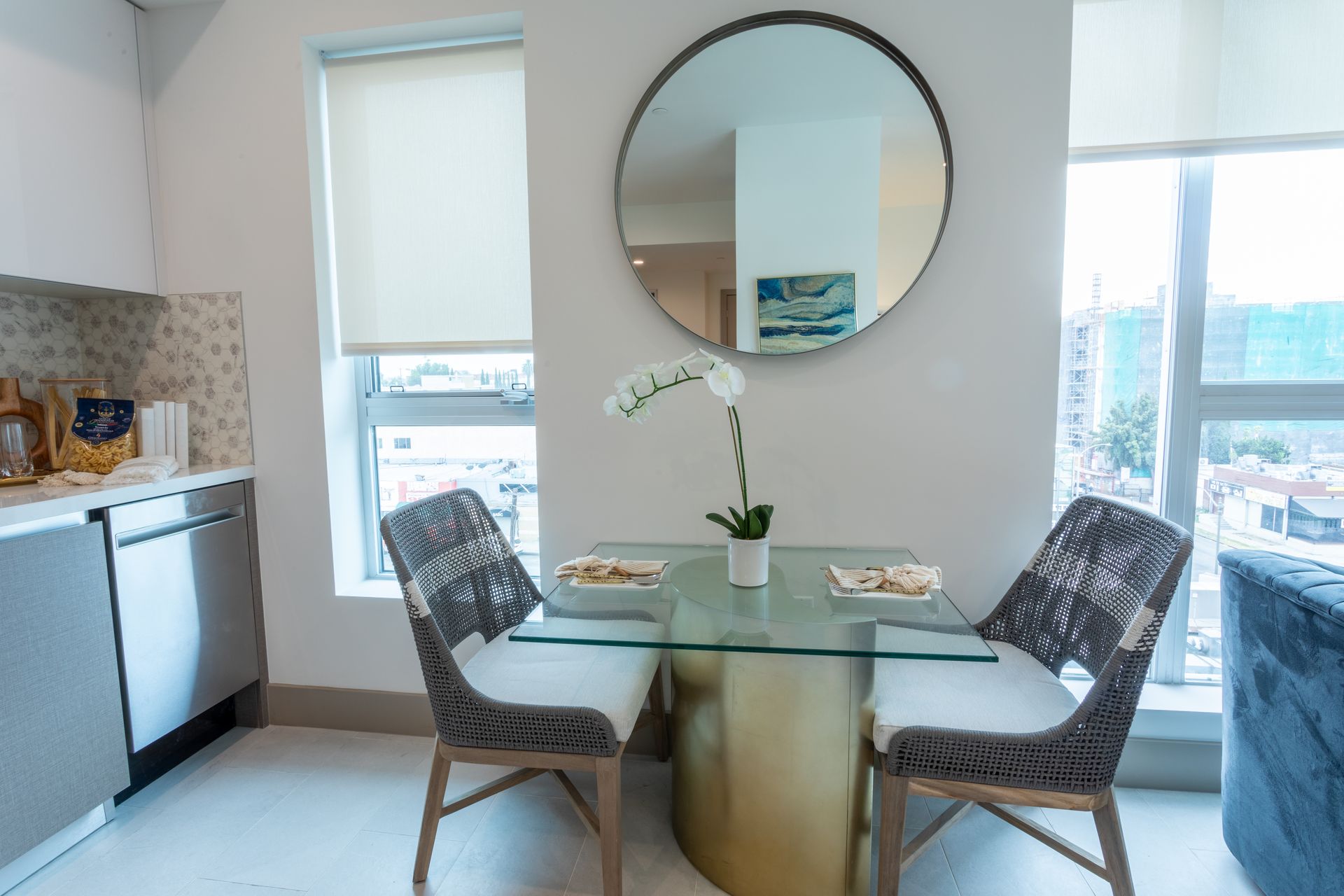 Dining area with a glass table, two chairs, a round mirror, and a window.