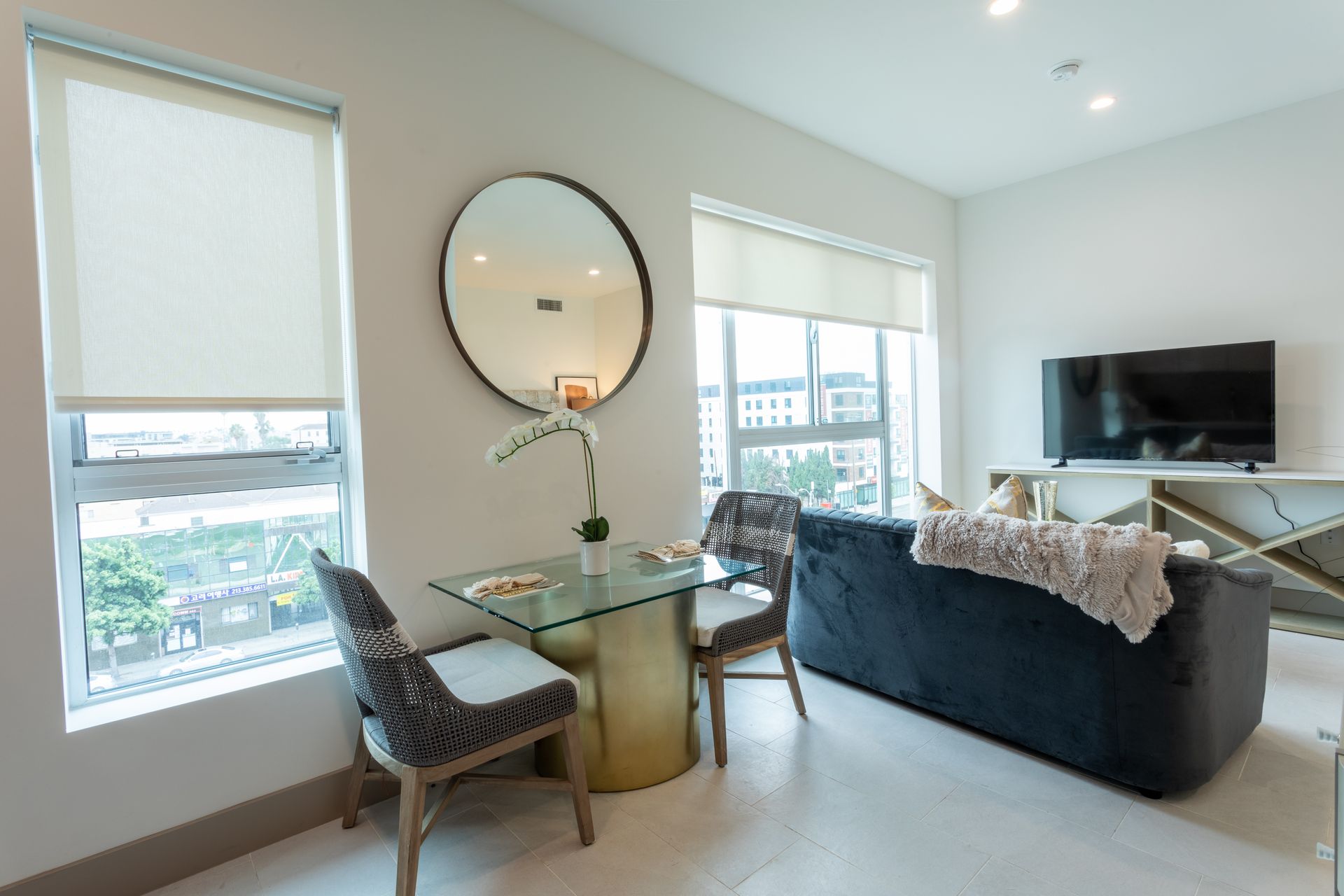 Modern living room with blue couch, round mirror, small glass table, and large windows.