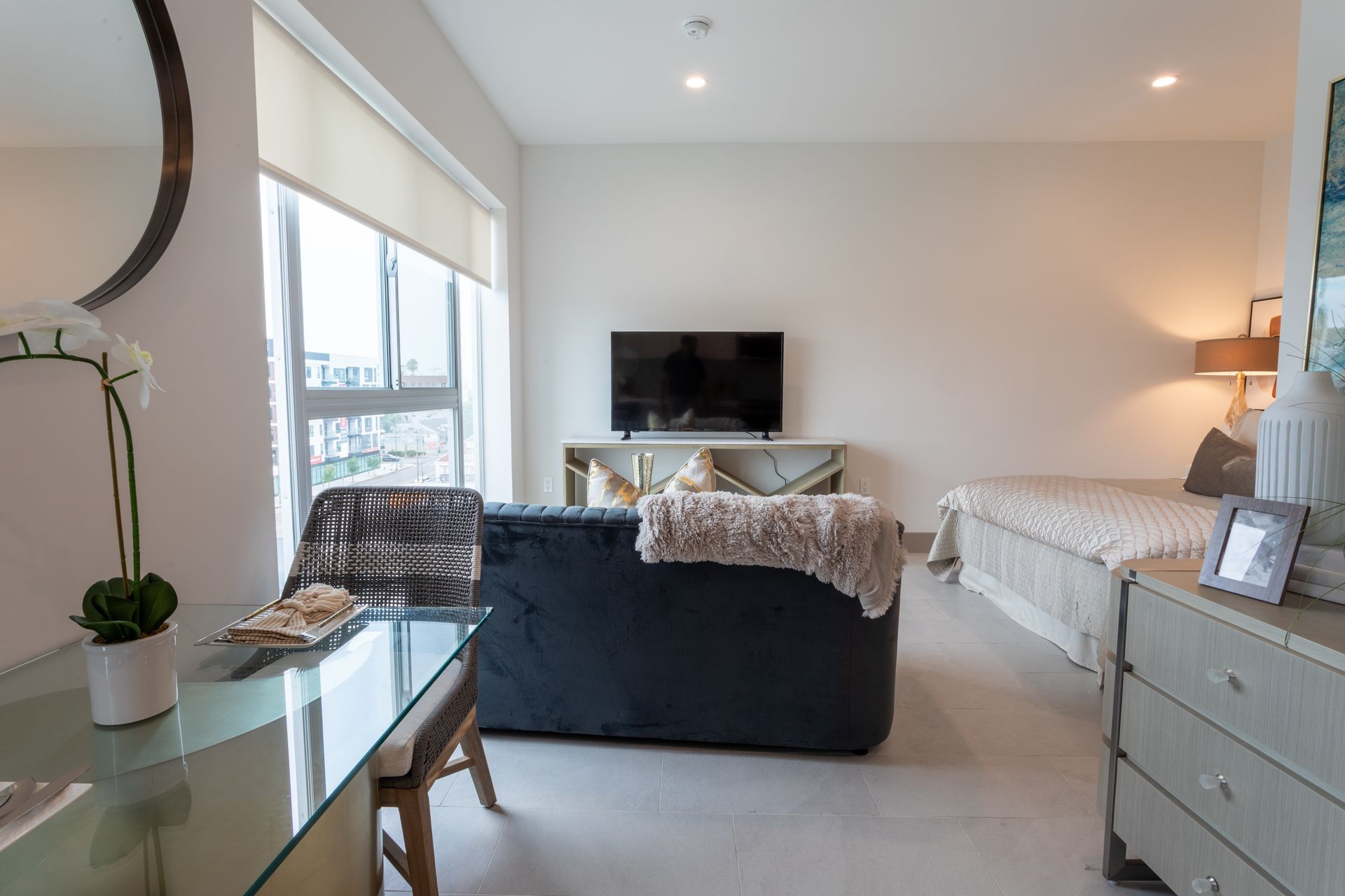 Modern studio apartment with a couch, bed, desk, and TV. Bright, neutral color scheme.