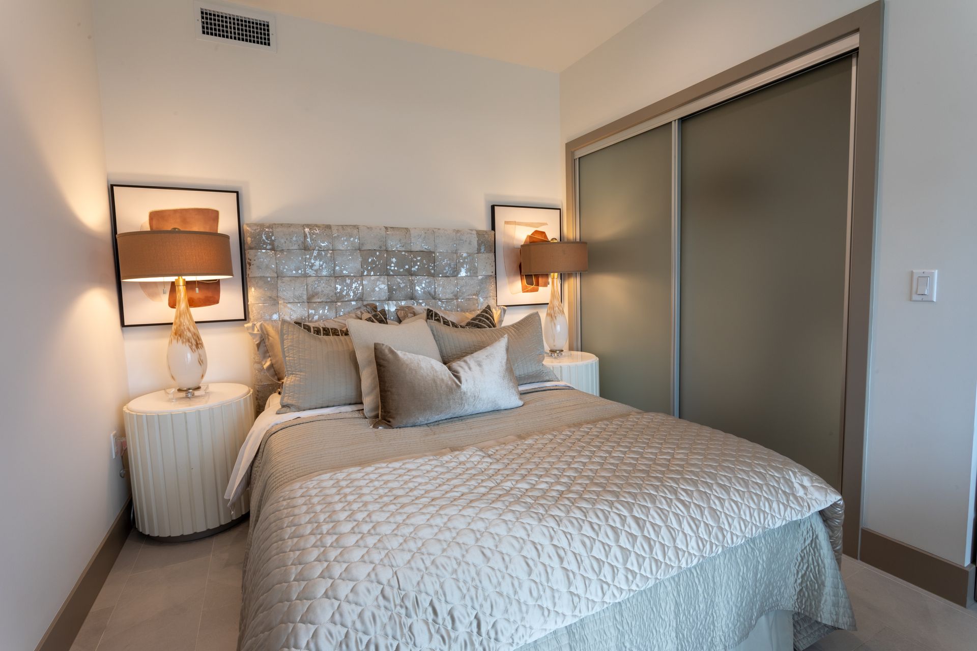 Bedroom with bed, bedside tables, lamps, artwork, and a sliding closet door.