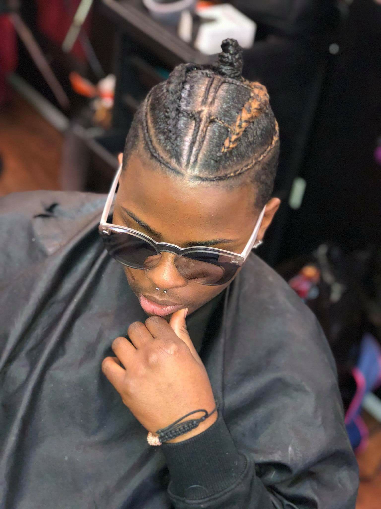 Person with braided hair bun, wearing sunglasses and a black cape, hands near face.