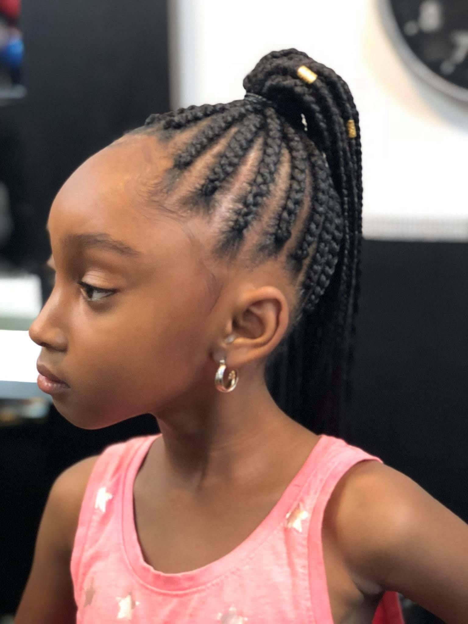 A little girl with braids in her hair is wearing a pink tank top.