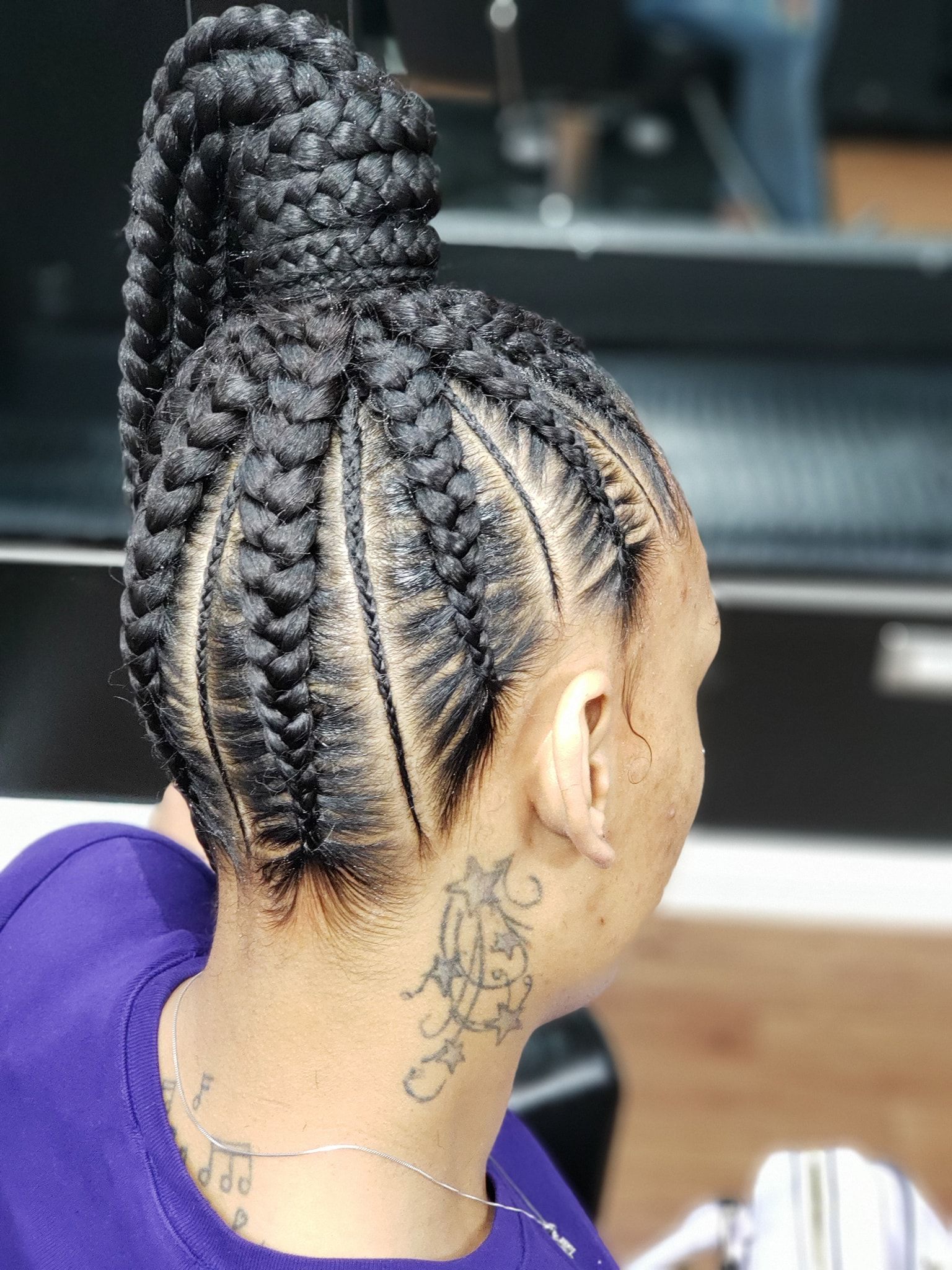 A woman with braids in a bun and a tattoo on her neck.