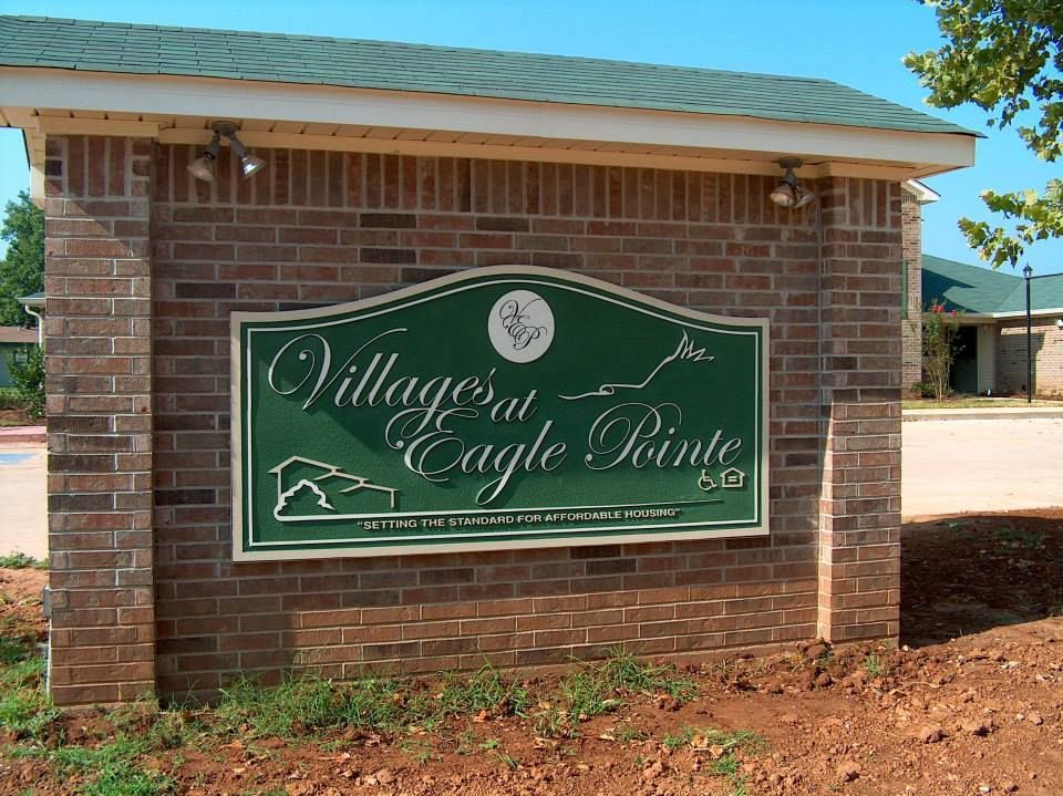 A green sign on a brick wall says village at eagle pointe
