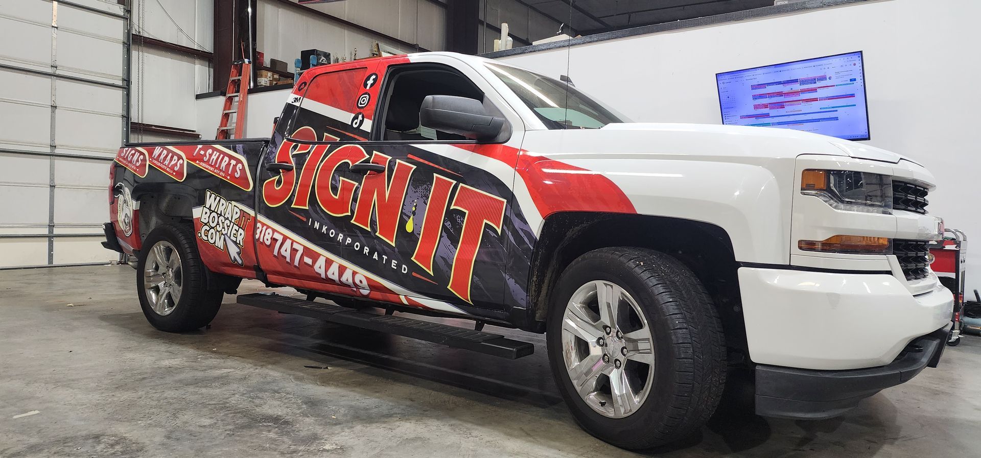 A white truck with a wrap on it is parked in a garage.
