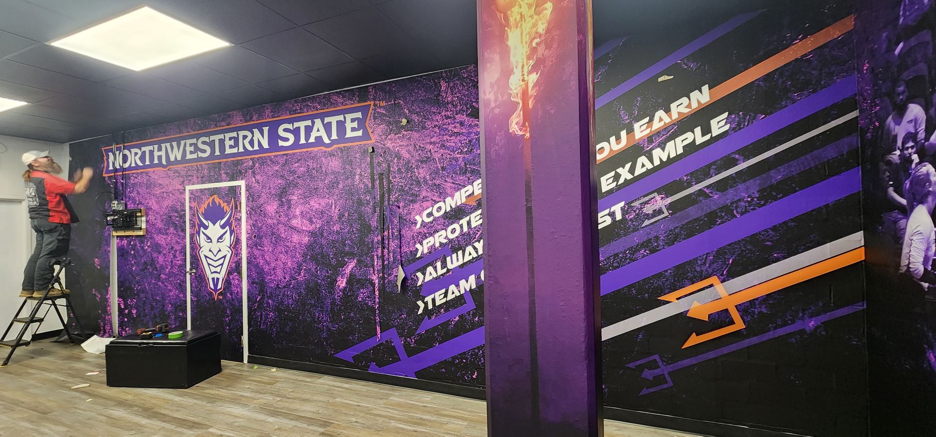 A man is standing on a ladder in front of a purple wall.