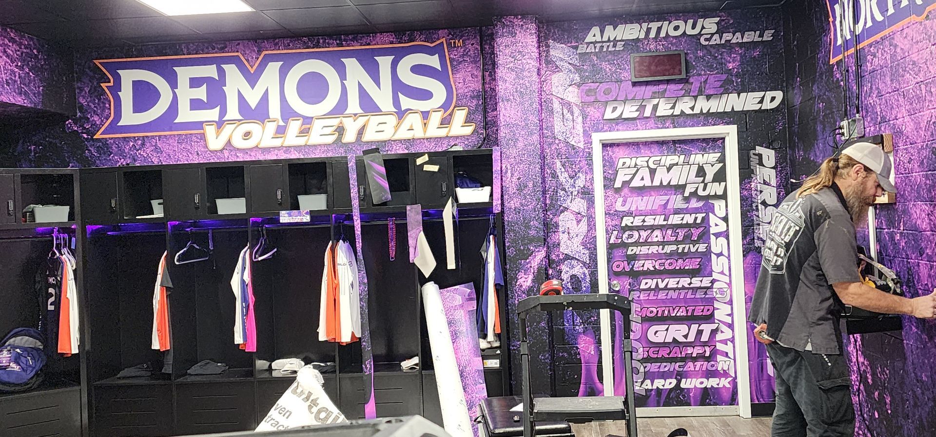 A man is standing in a locker room with a sign that says demons volleyball.