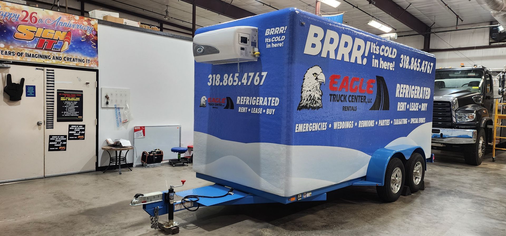 A blue and white trailer is parked in a garage next to a truck.
