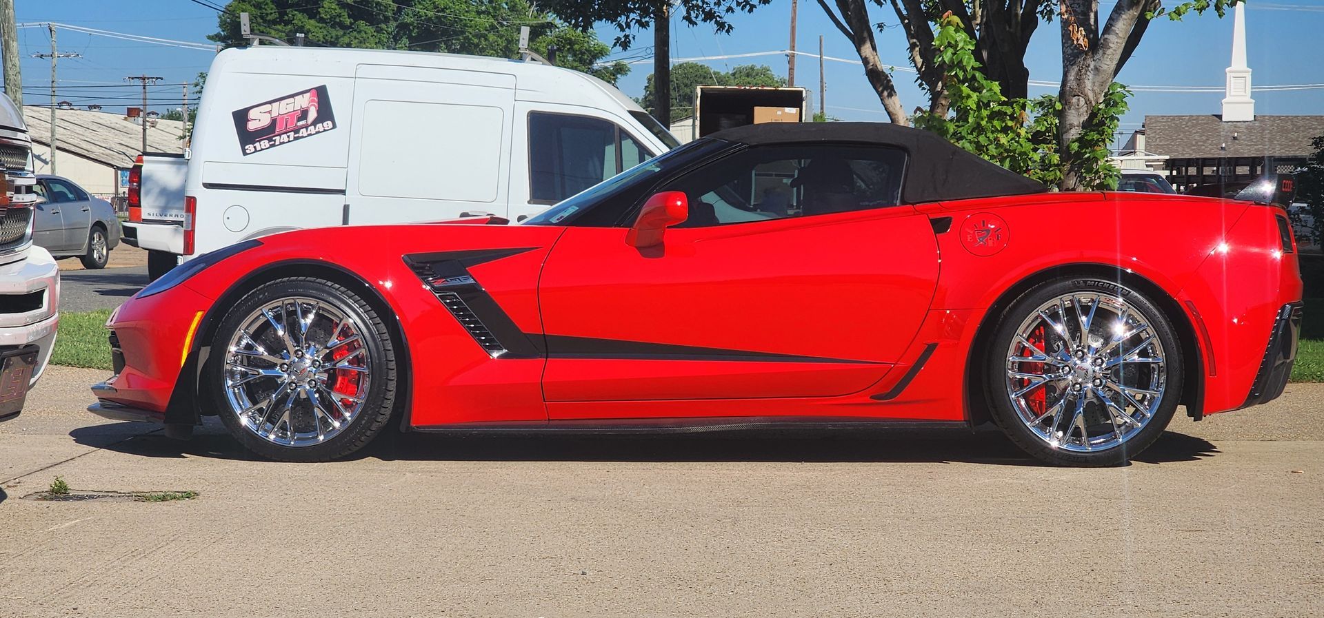A red sports car is parked in a parking lot next to a white van.