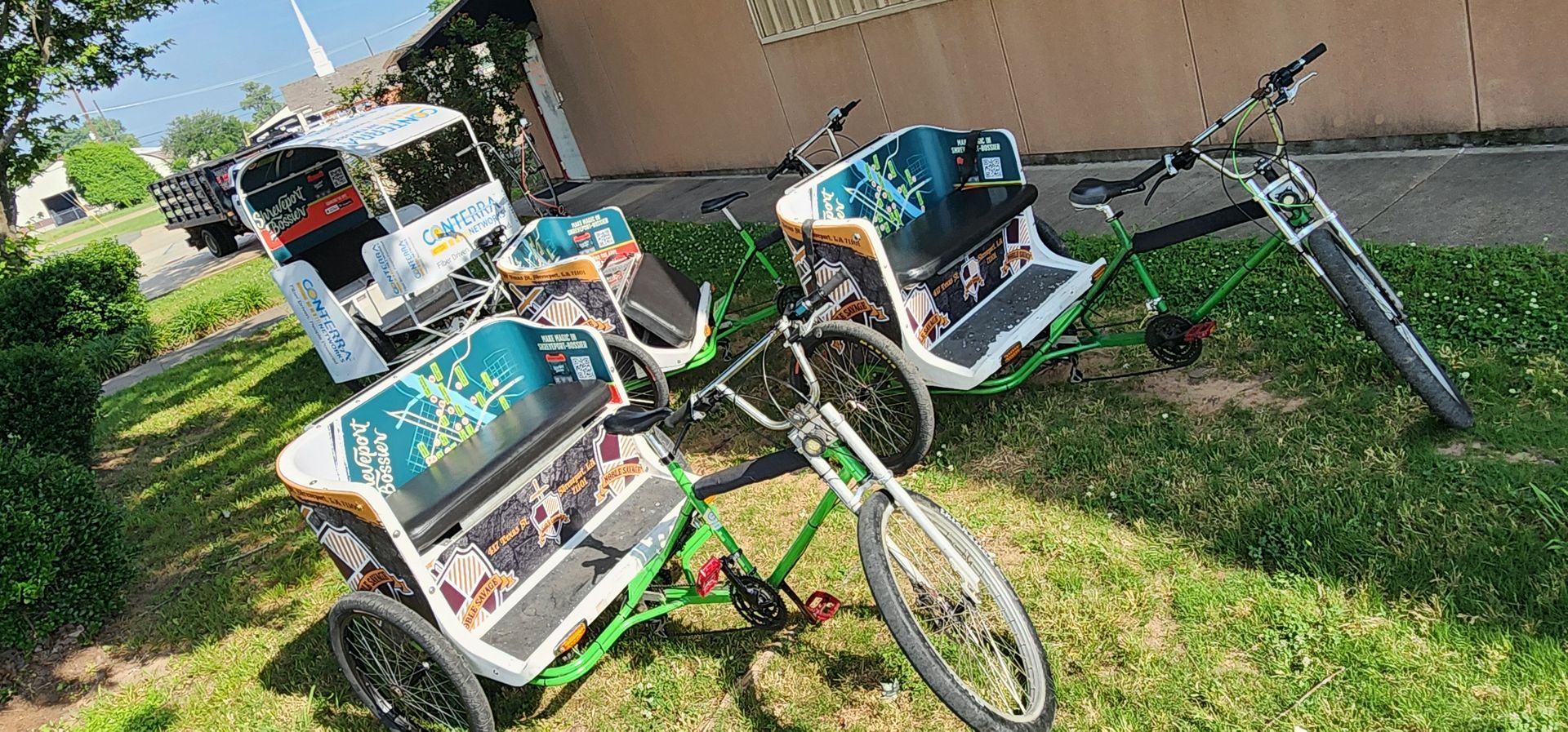 Three rickshaws are parked in the grass in front of a building.