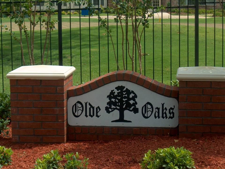 A sign for olde oaks sits in front of a fence