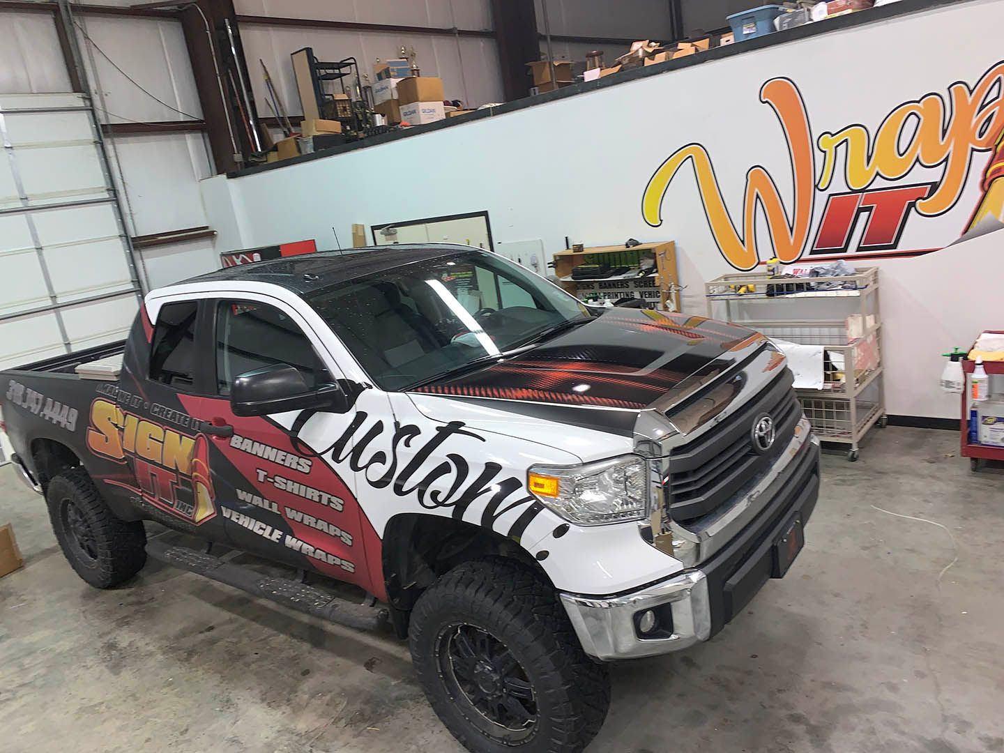 A truck with a wrap on it is parked in a garage.