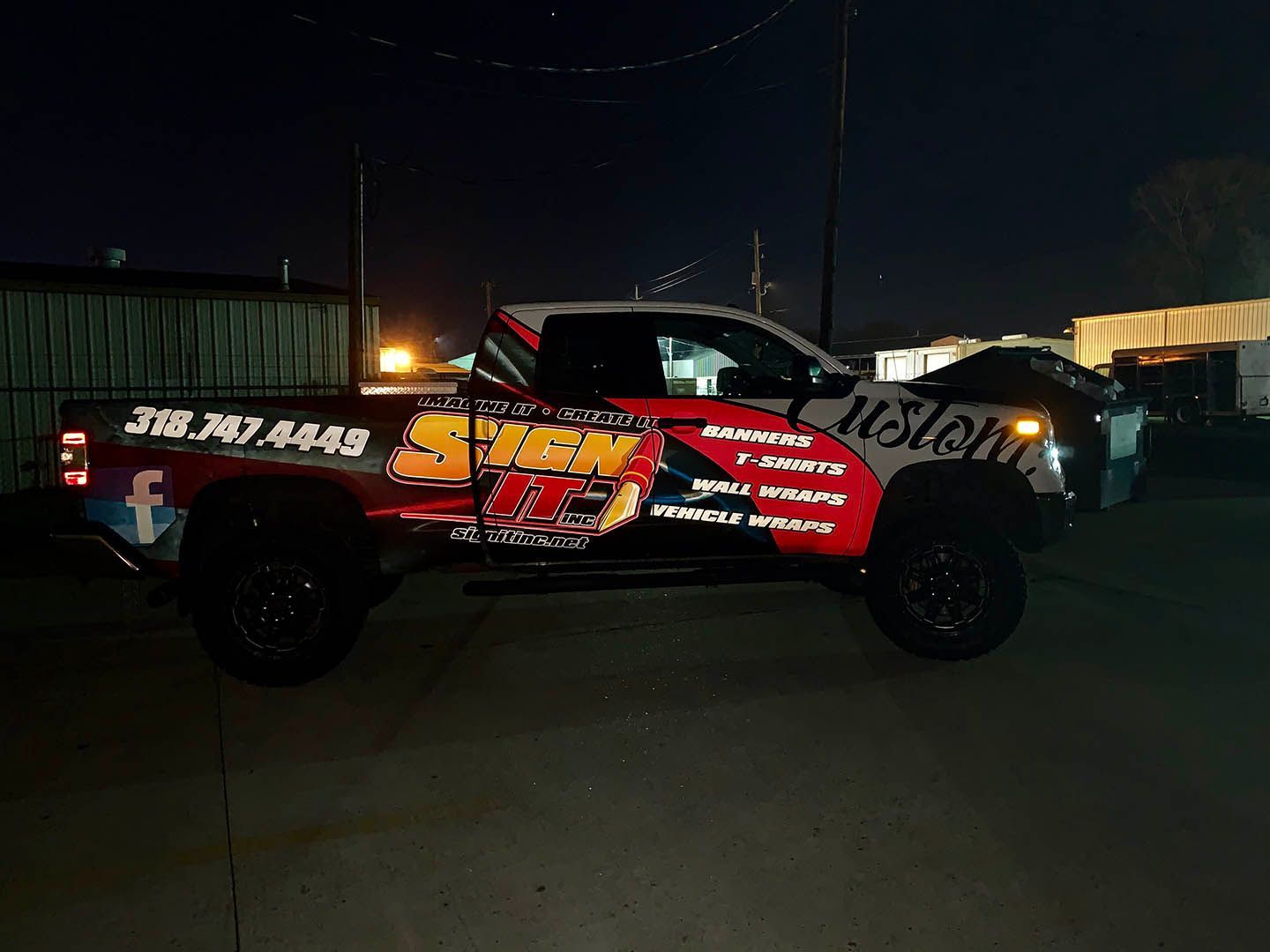 A red and black truck is parked in a parking lot at night.