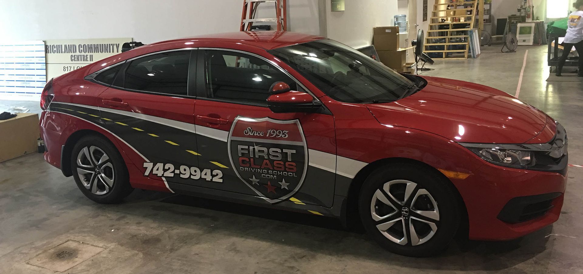 A red car with a wrap on it is parked in a garage.