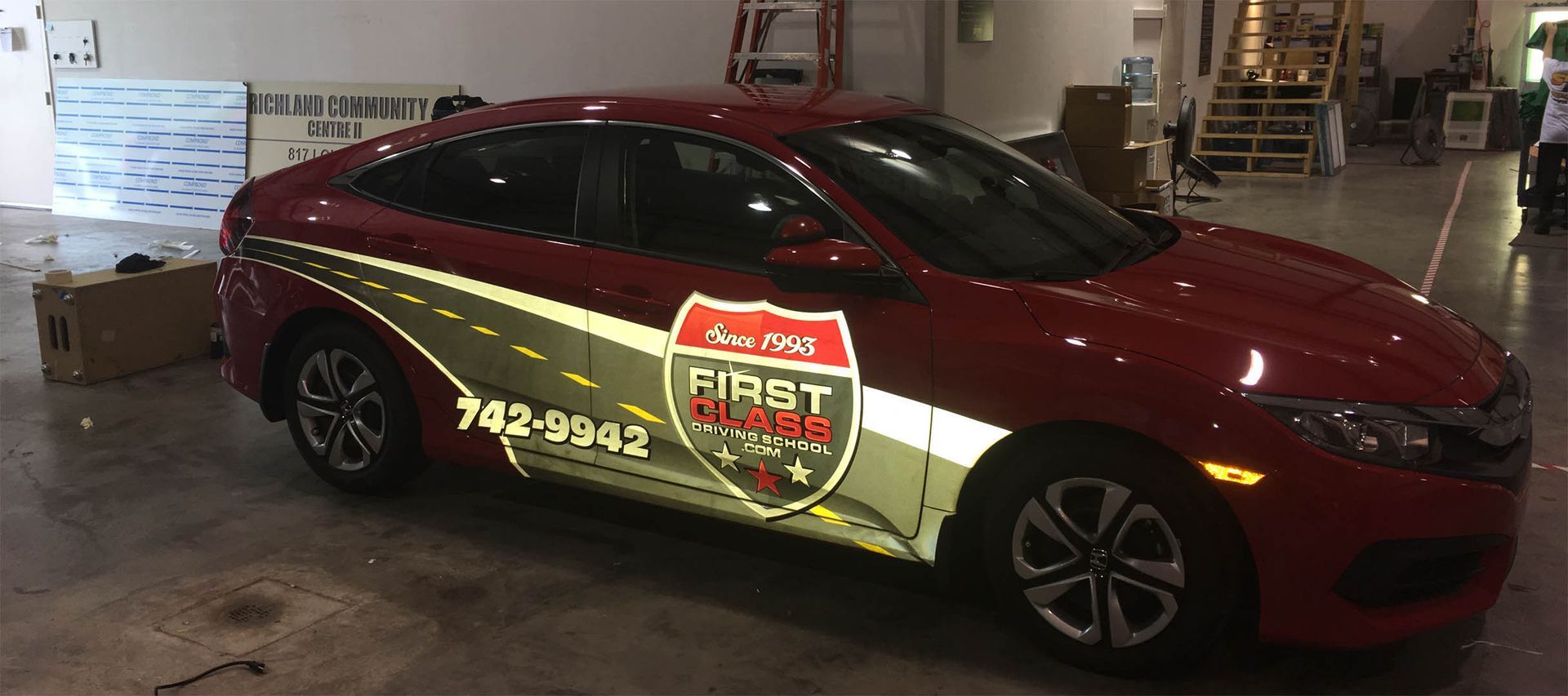 A red car with a wrap on it is parked in a garage.