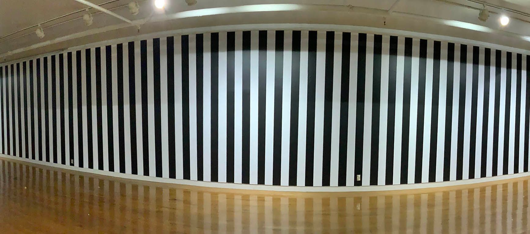 A large black and white striped wall in a room with a wooden floor.