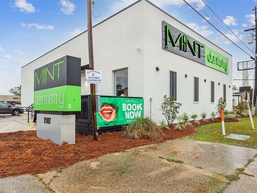 A white building with a green sign that says mint dentistry
