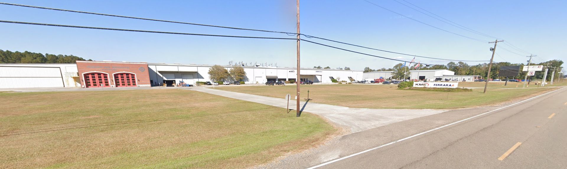 A road going through a grassy field with a building in the background.
