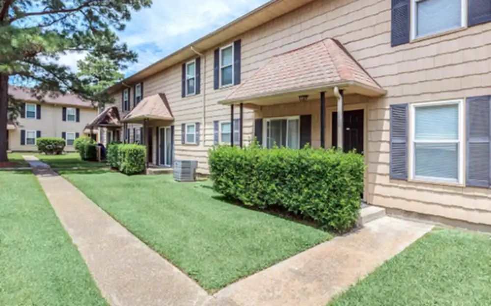A row of apartment buildings with a lush green lawn in front of them.