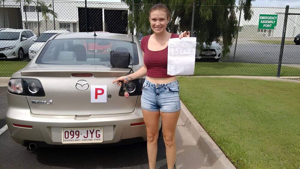 A Woman Is Standing In Front Of A Car With A License Plate — Solitude Driving School In Mooroobool, QLD