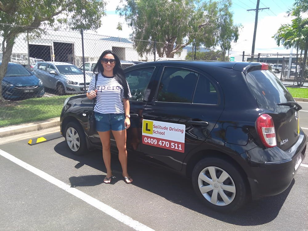 A Woman Is Standing In Front Of A Black Car That Says L On It — Solitude Driving School In Mooroobool, QLD