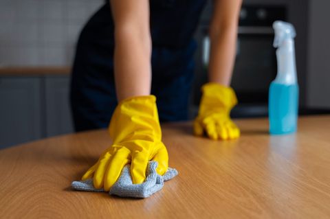 A person wearing yellow gloves is cleaning a wooden table with a cloth.