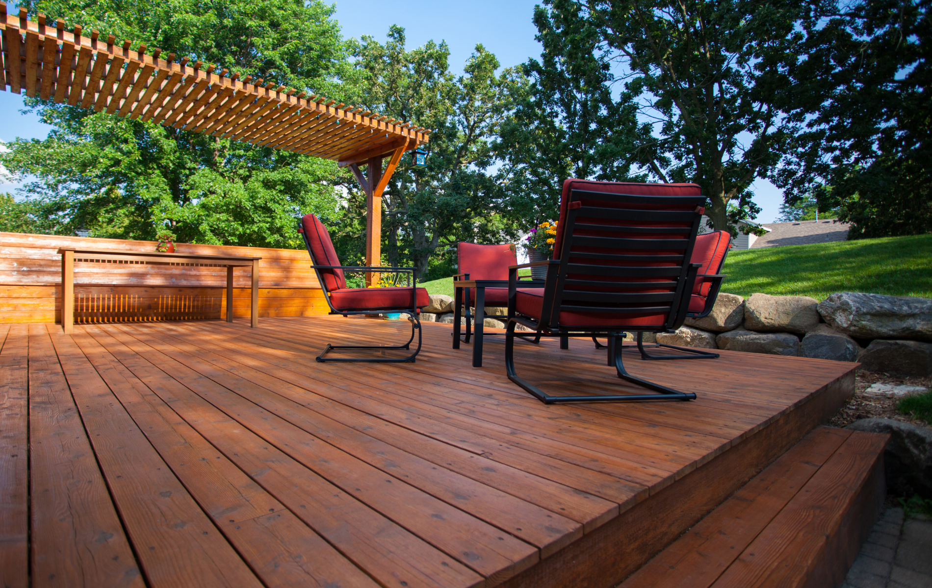 A wooden deck with chairs and a table under a pergola.