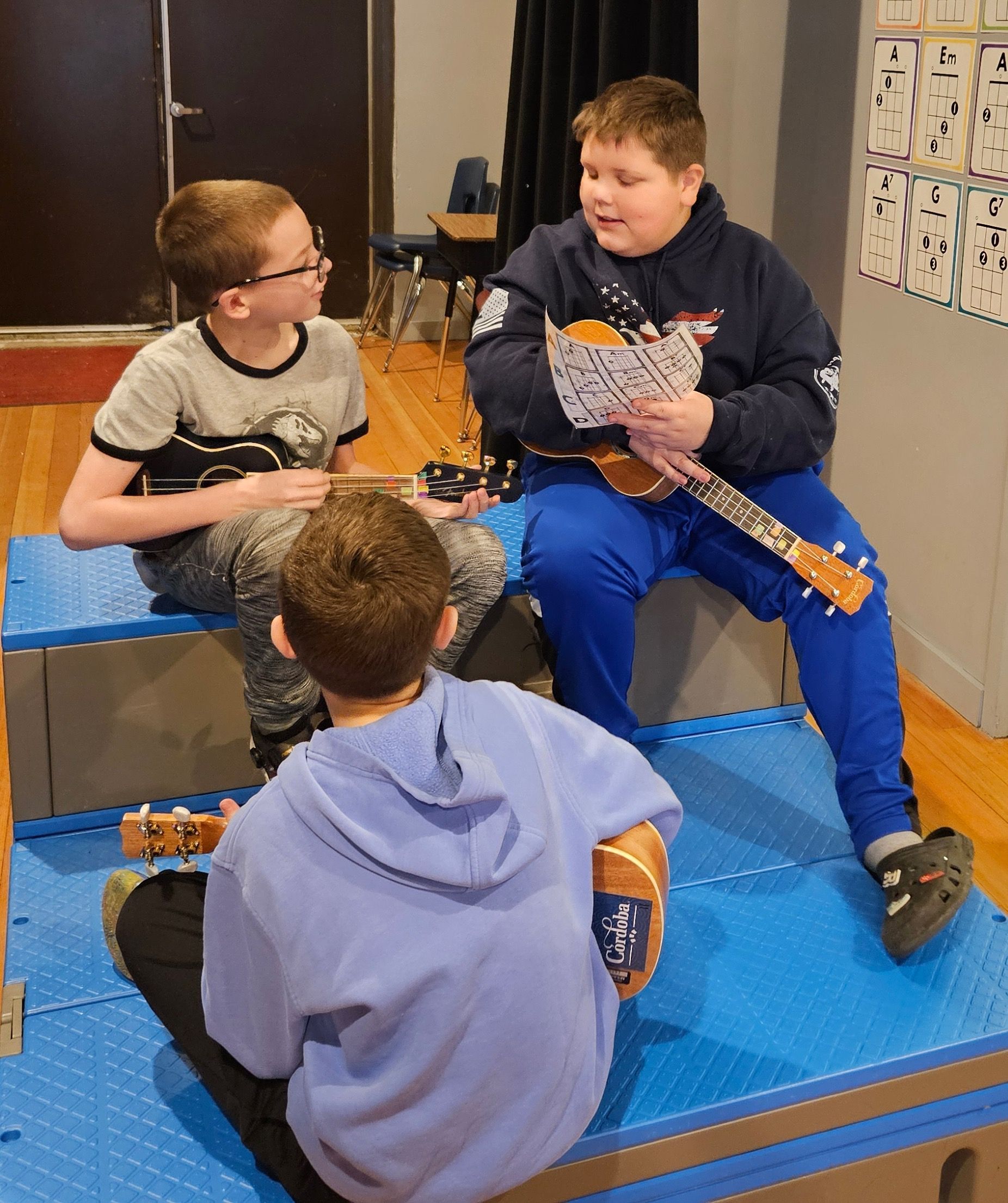 A boy in a blue hoodie is playing a guitar