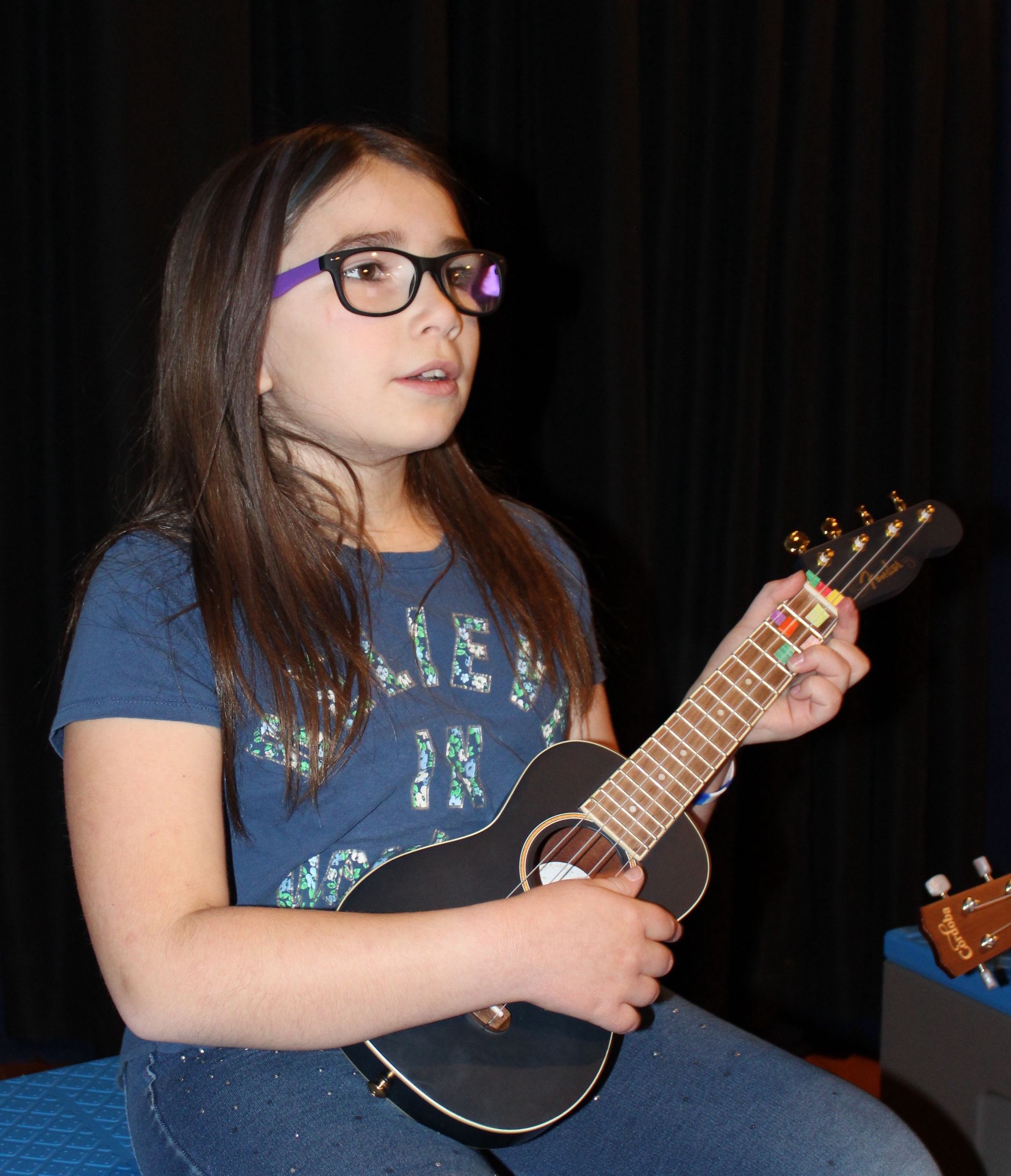 A young girl wearing glasses is playing an ukulele