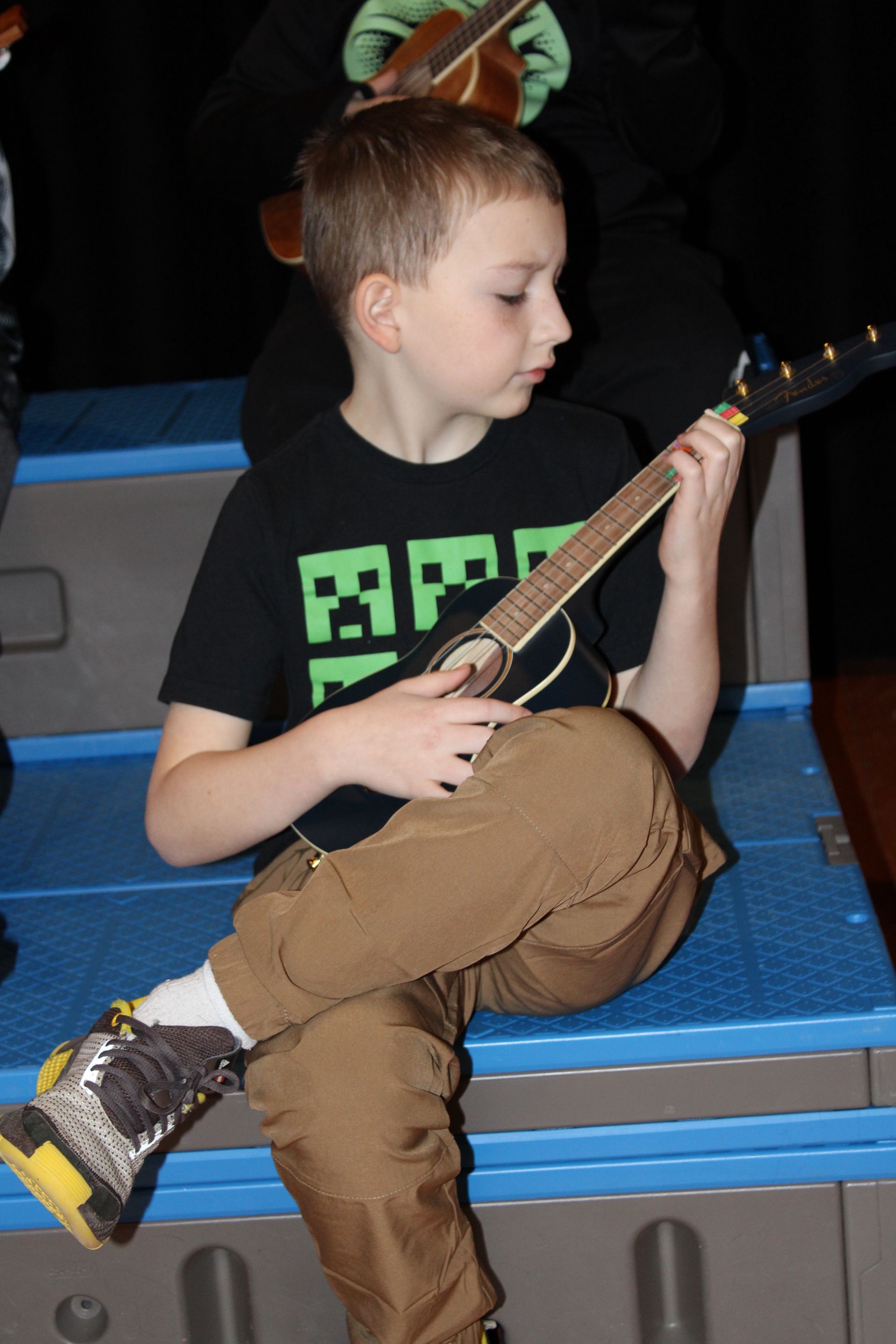 A young boy wearing a black shirt that says bf is playing a guitar