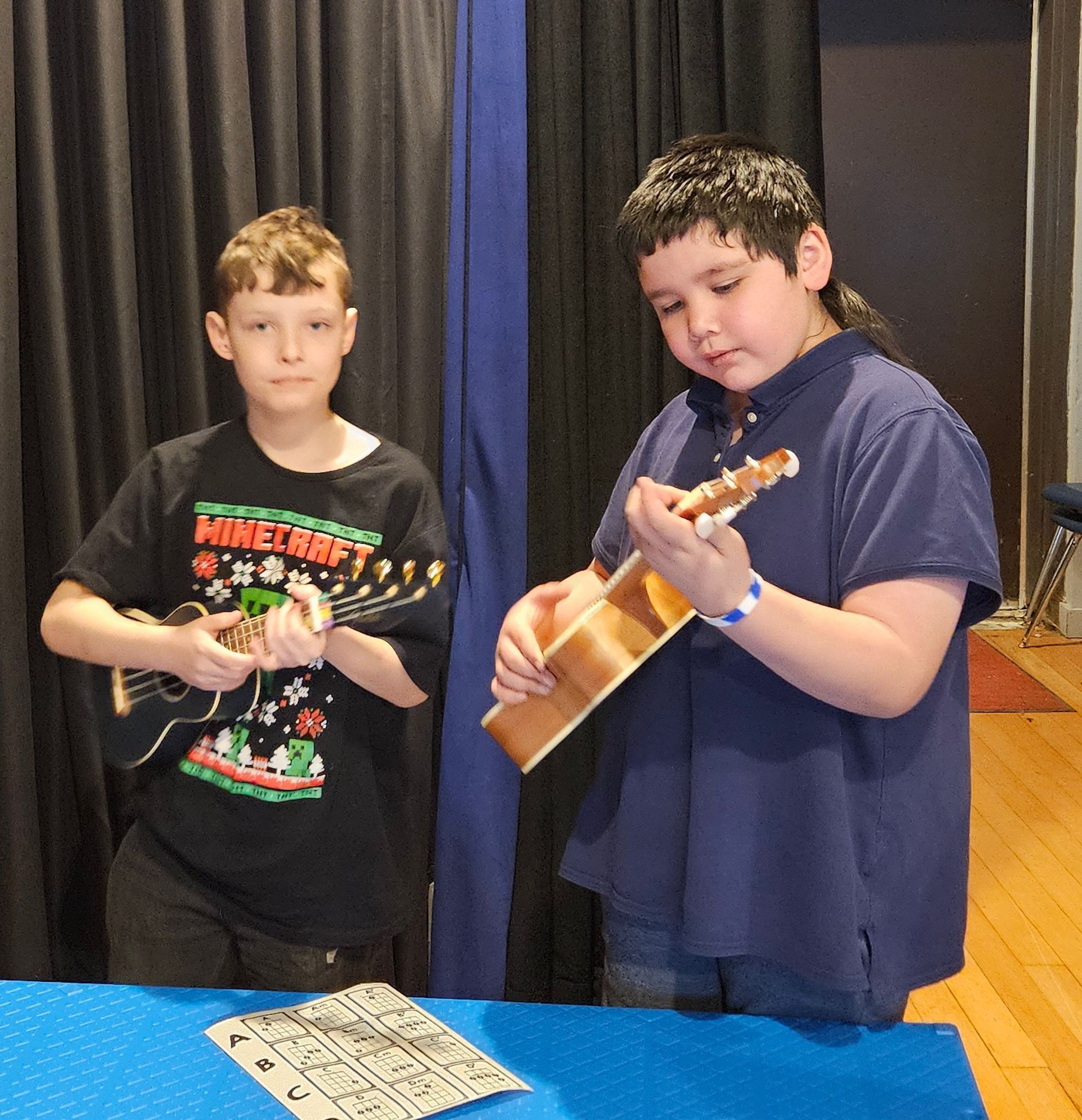 A boy wearing a minecraft shirt is playing a guitar