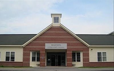 The front of a brick building with a black roof and a sign that says madison elementary school.