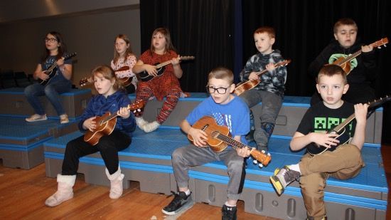 A group of children are sitting on a stage playing guitars.