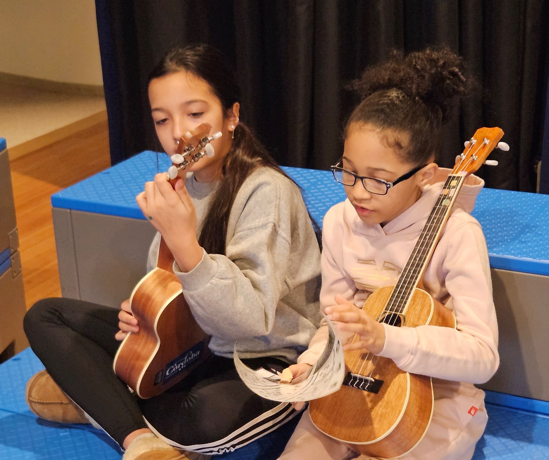 Two girls are sitting on the floor playing guitars