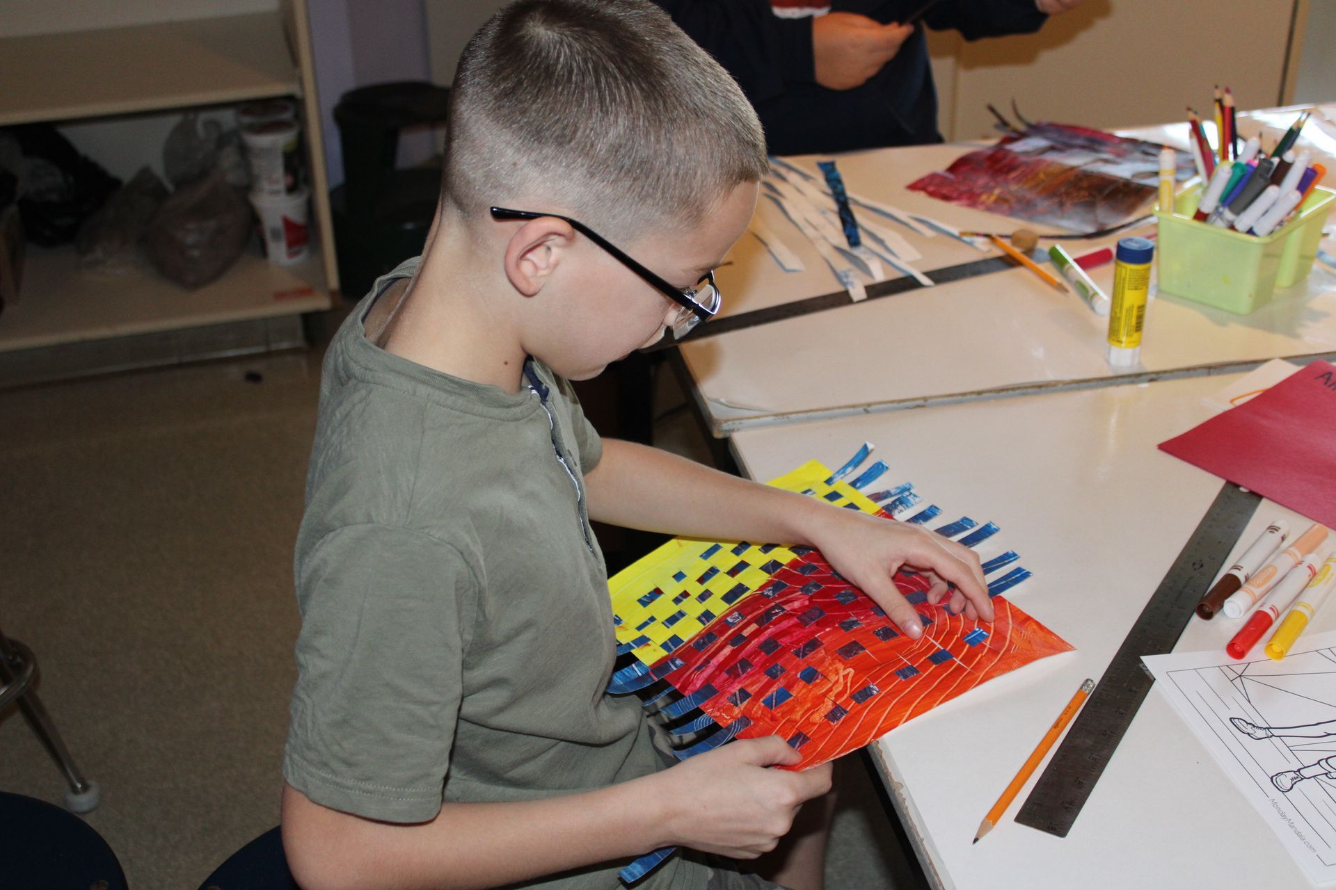 A boy wearing glasses sits at a table working on a project