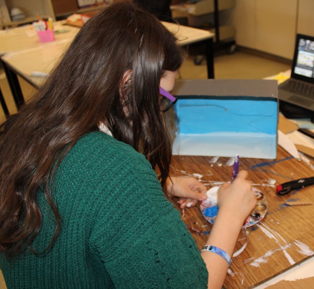 A girl in a green sweater sits at a table with a laptop