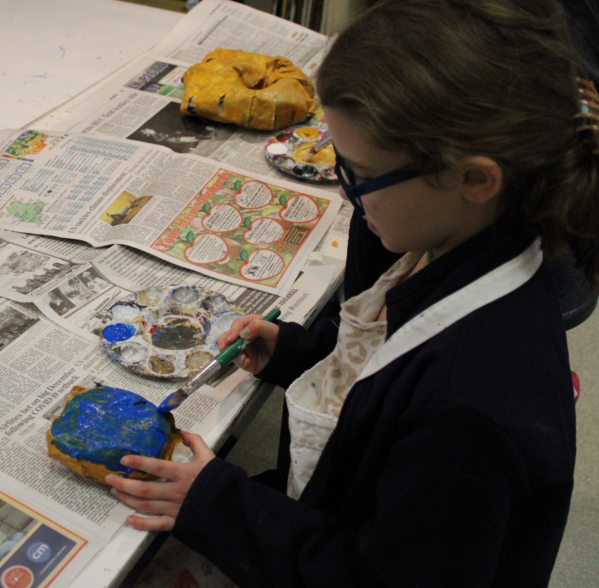 A young girl is painting a pumpkin with blue paint