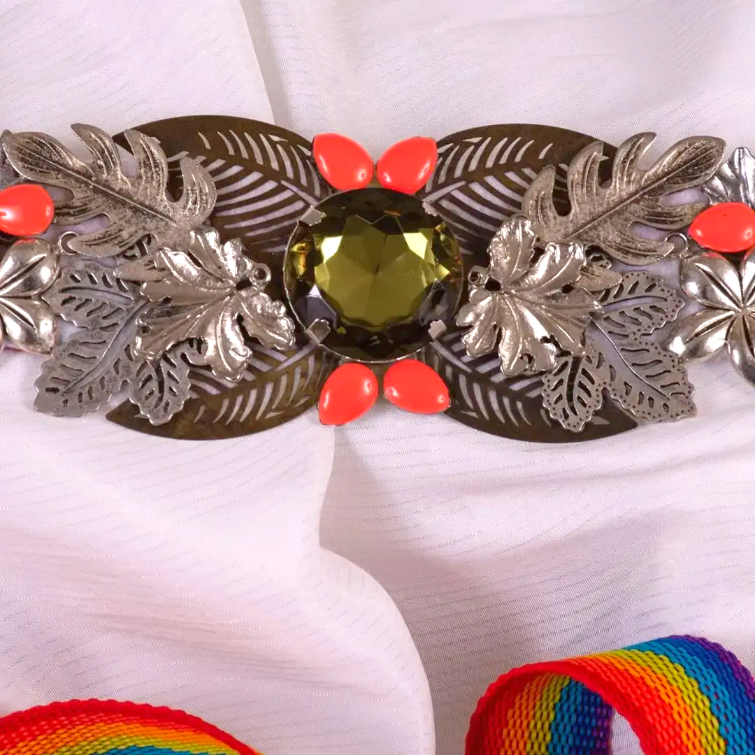 Cinturón metálico con piedra oliva, cuentas de coral y detalles de pan de plata sobre tela blanca.