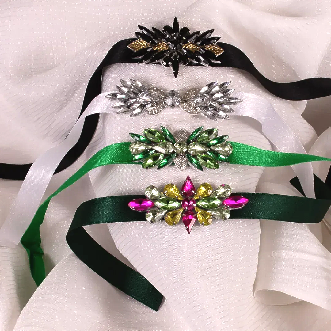Cuatro diademas de cintas con joyas, de color negro, blanco, verde y verde oscuro, dispuestas sobre tela blanca.