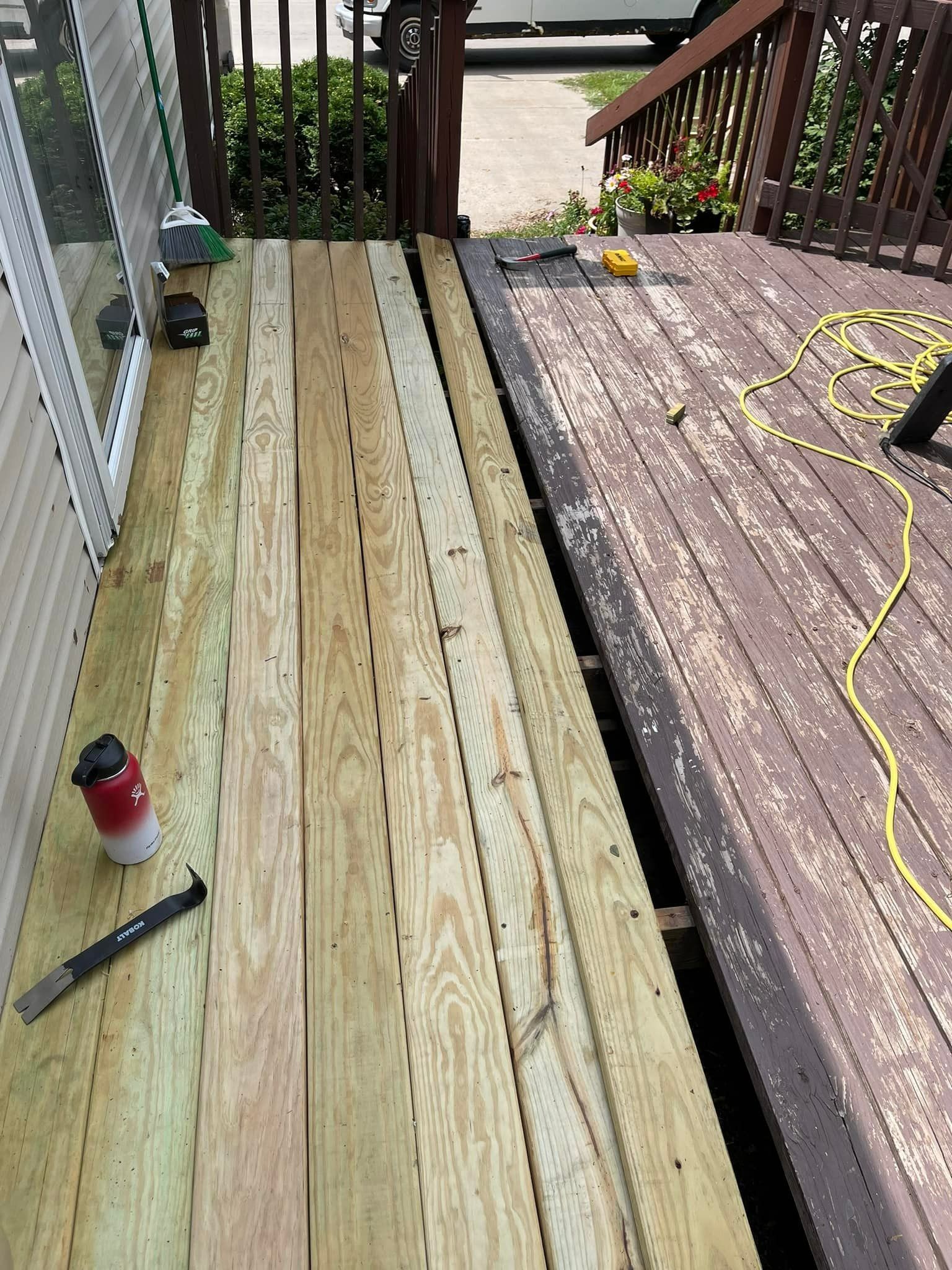 Deck partially renovated, showing old weathered planks next to new, lighter wood. Tools, yellow cord present.