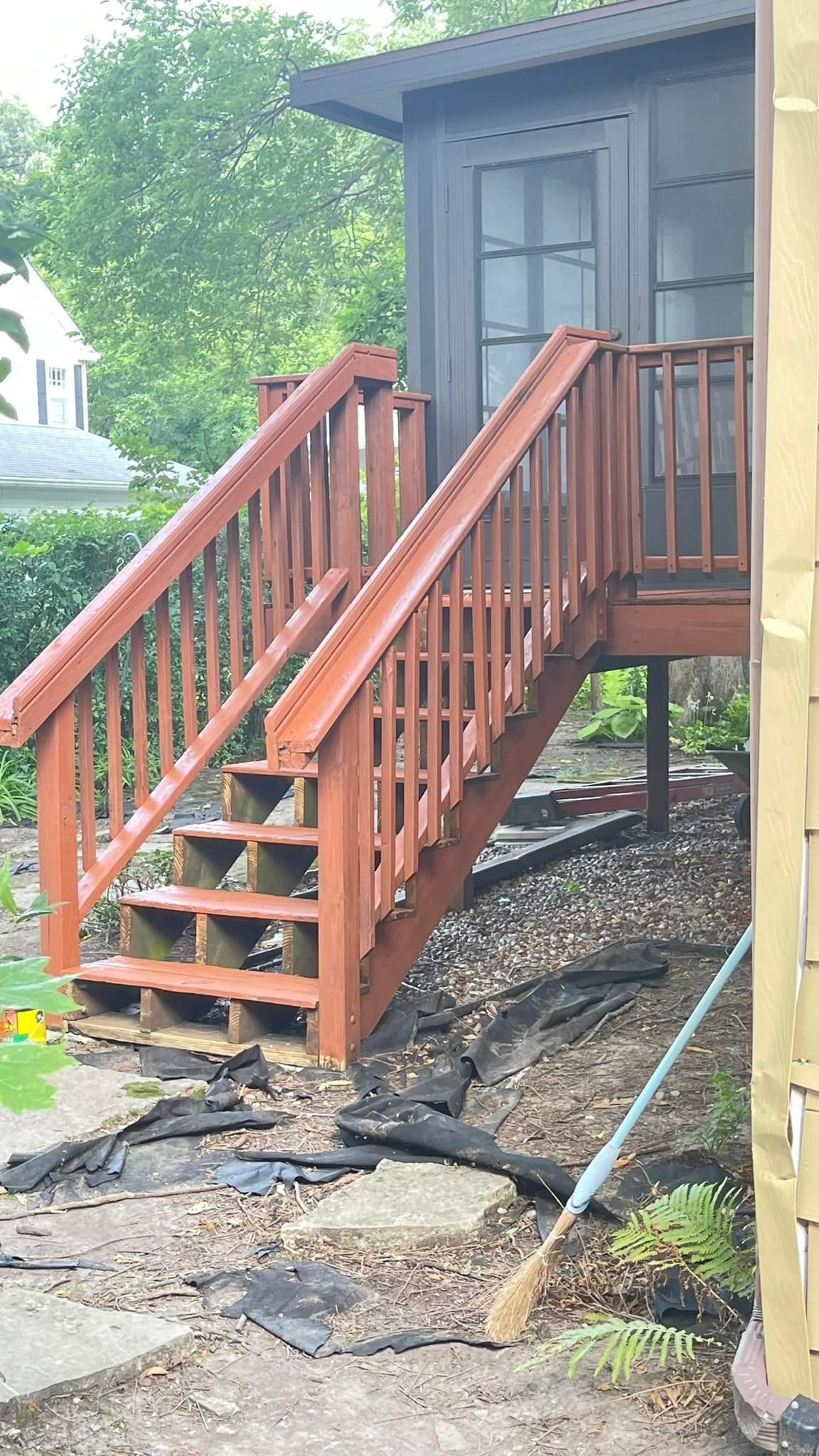 Wooden outdoor staircase with red railing, leading up to a dark-colored structure.