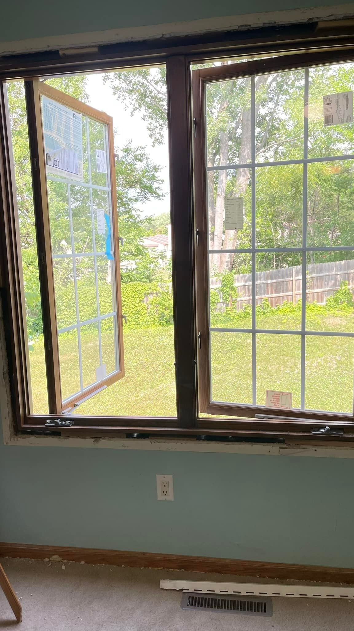 Open window with a grid pattern, brown frame. Partially opened to a green backyard on a blue-painted wall.