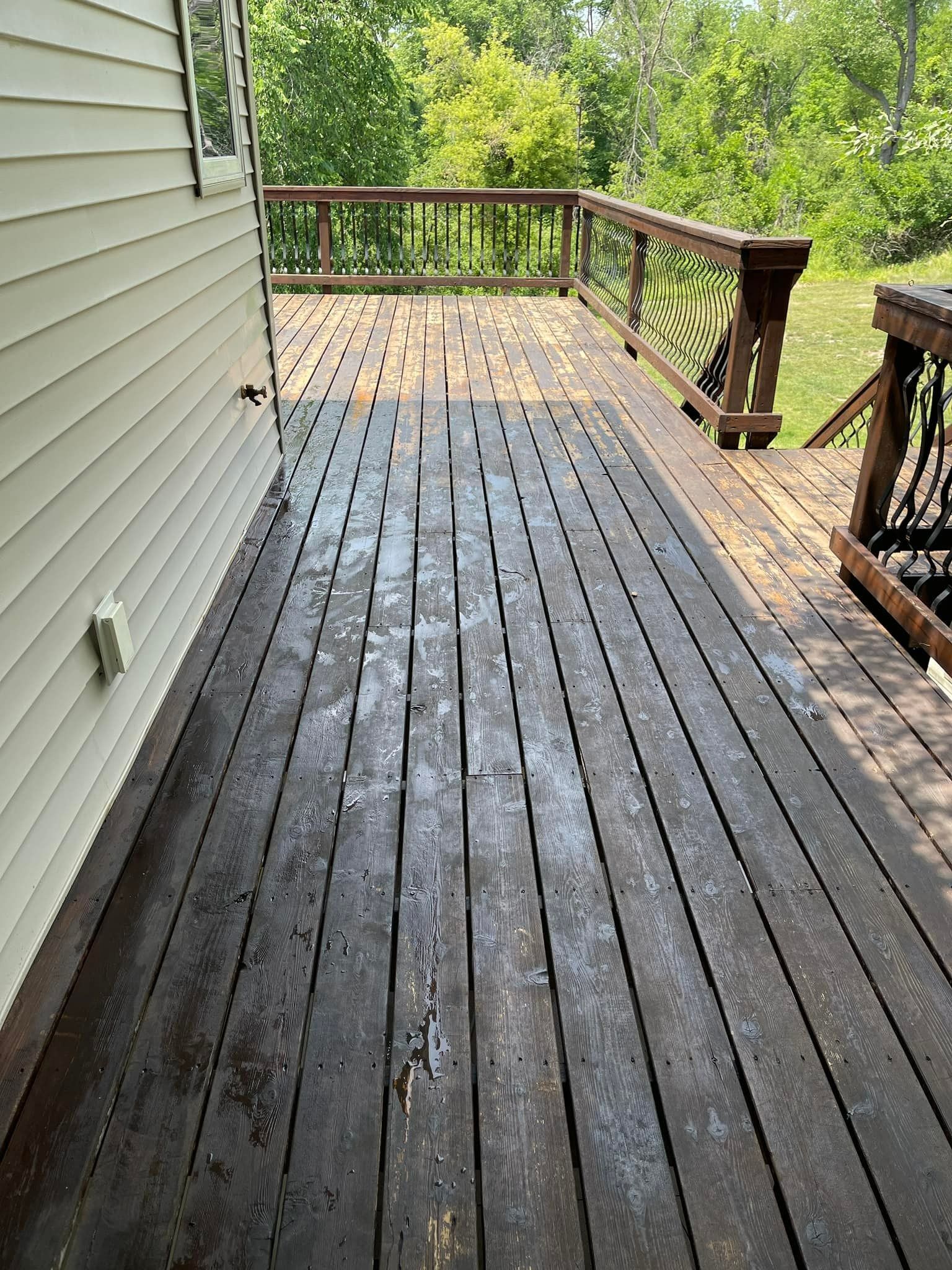 Wooden deck extending from a house with a dark stain. Trees and railings are in the background.