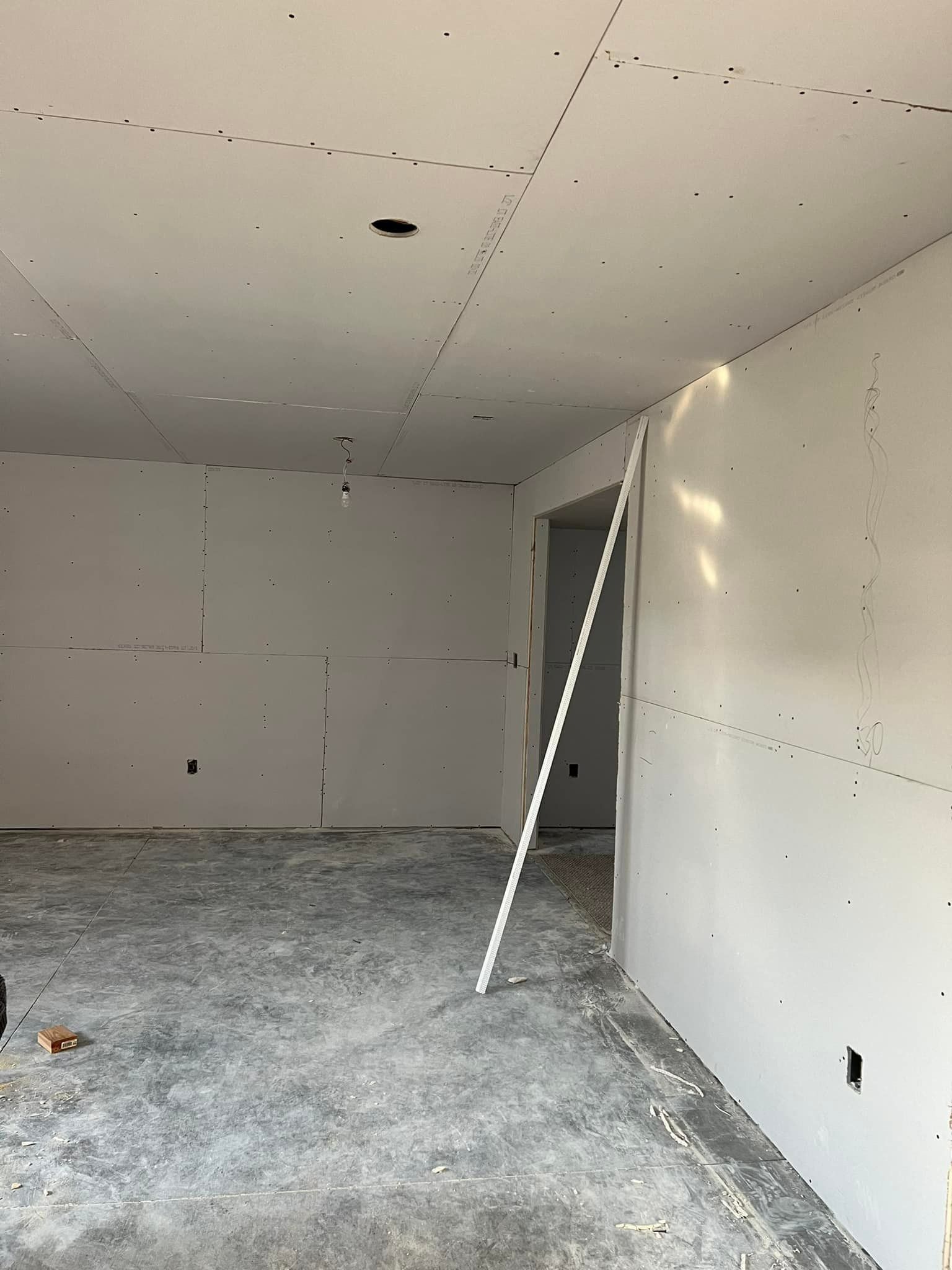 Interior room under construction, drywall on walls and ceiling, bare concrete floor, doorway.