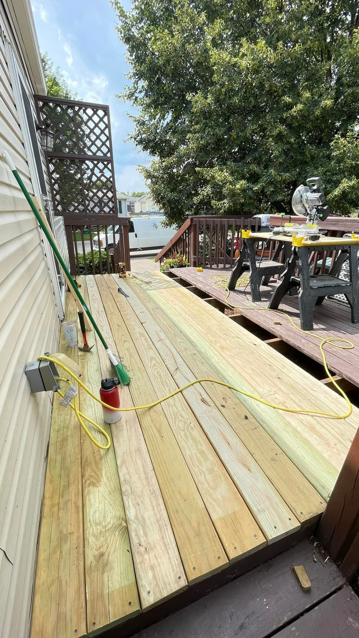Wooden deck under construction next to a house with tools and power cords visible.