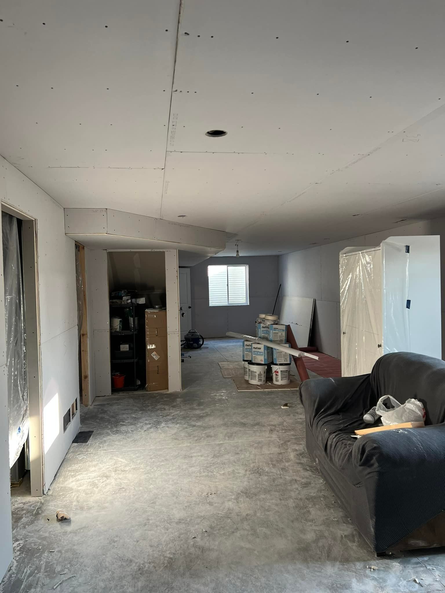 Room under construction with exposed drywall and a couch; cement floor.