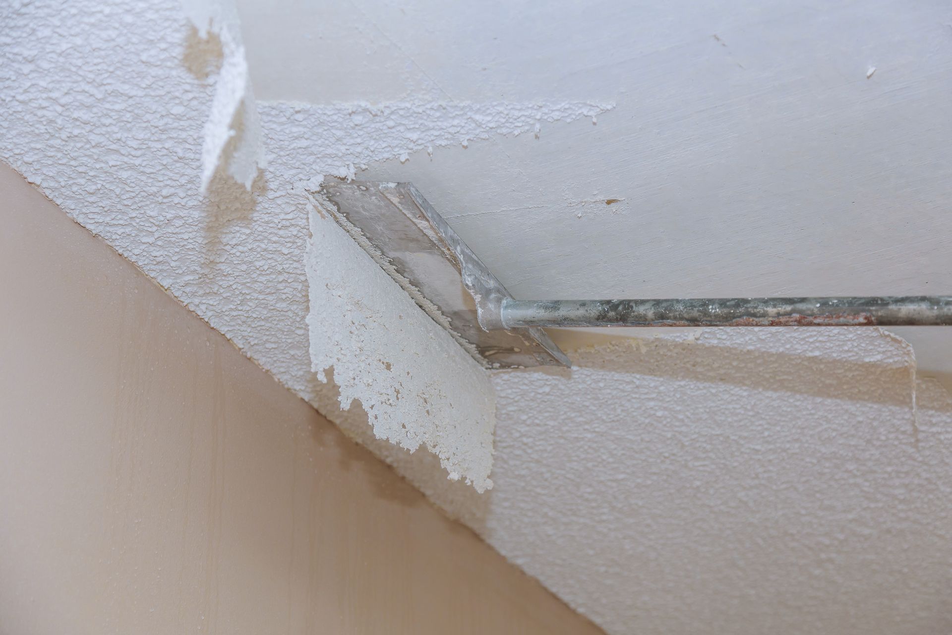 Applying textured ceiling coating with a tool; white, indoor setting.