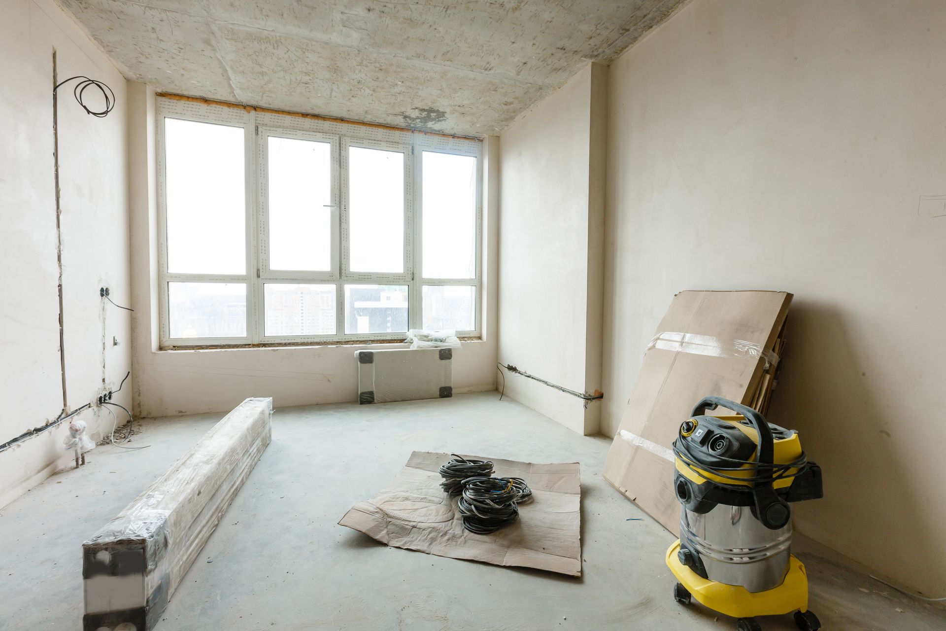 Empty room under construction with window, vacuum cleaner, and materials.