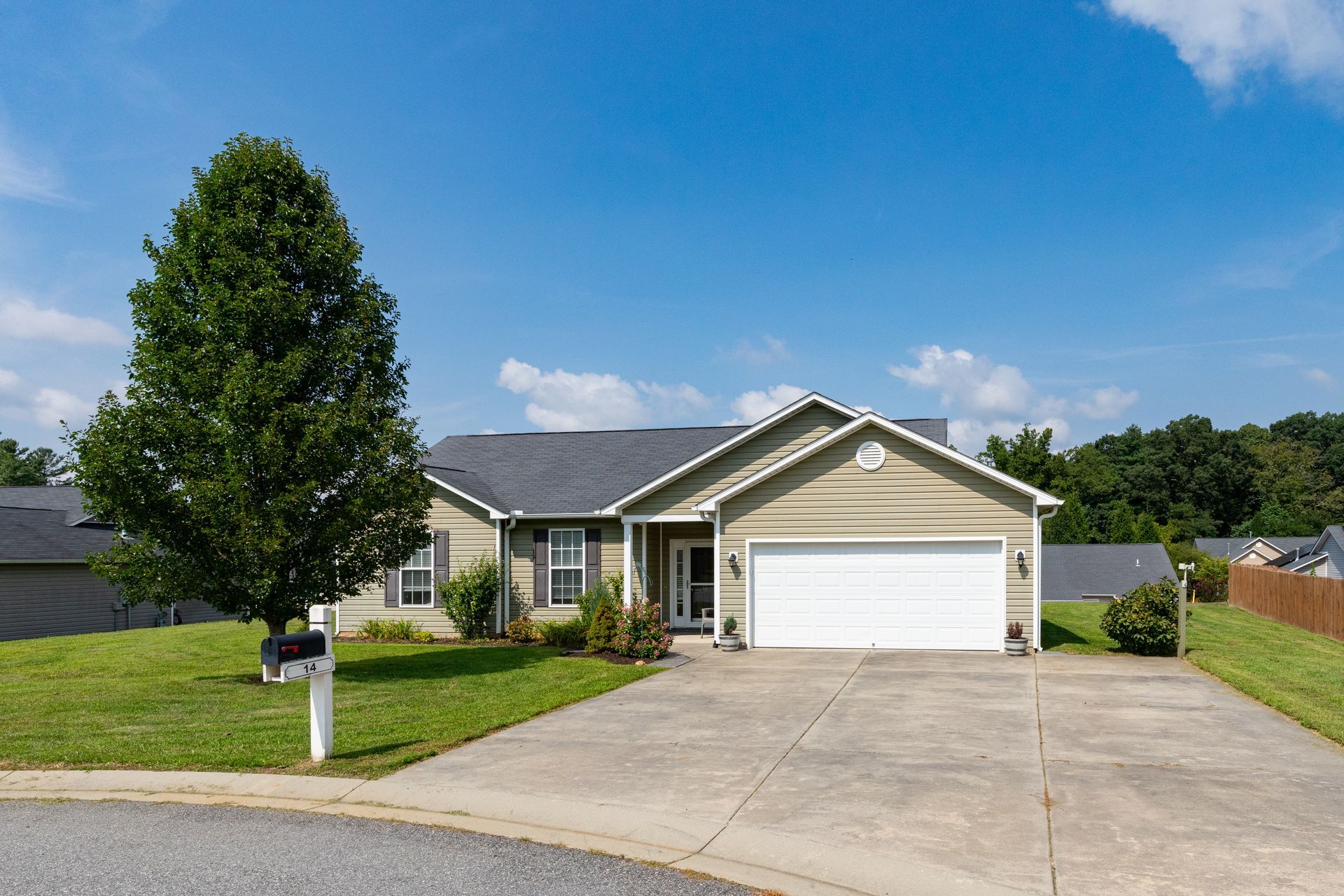 House with light green siding, white garage door, and green lawn on a sunny day.