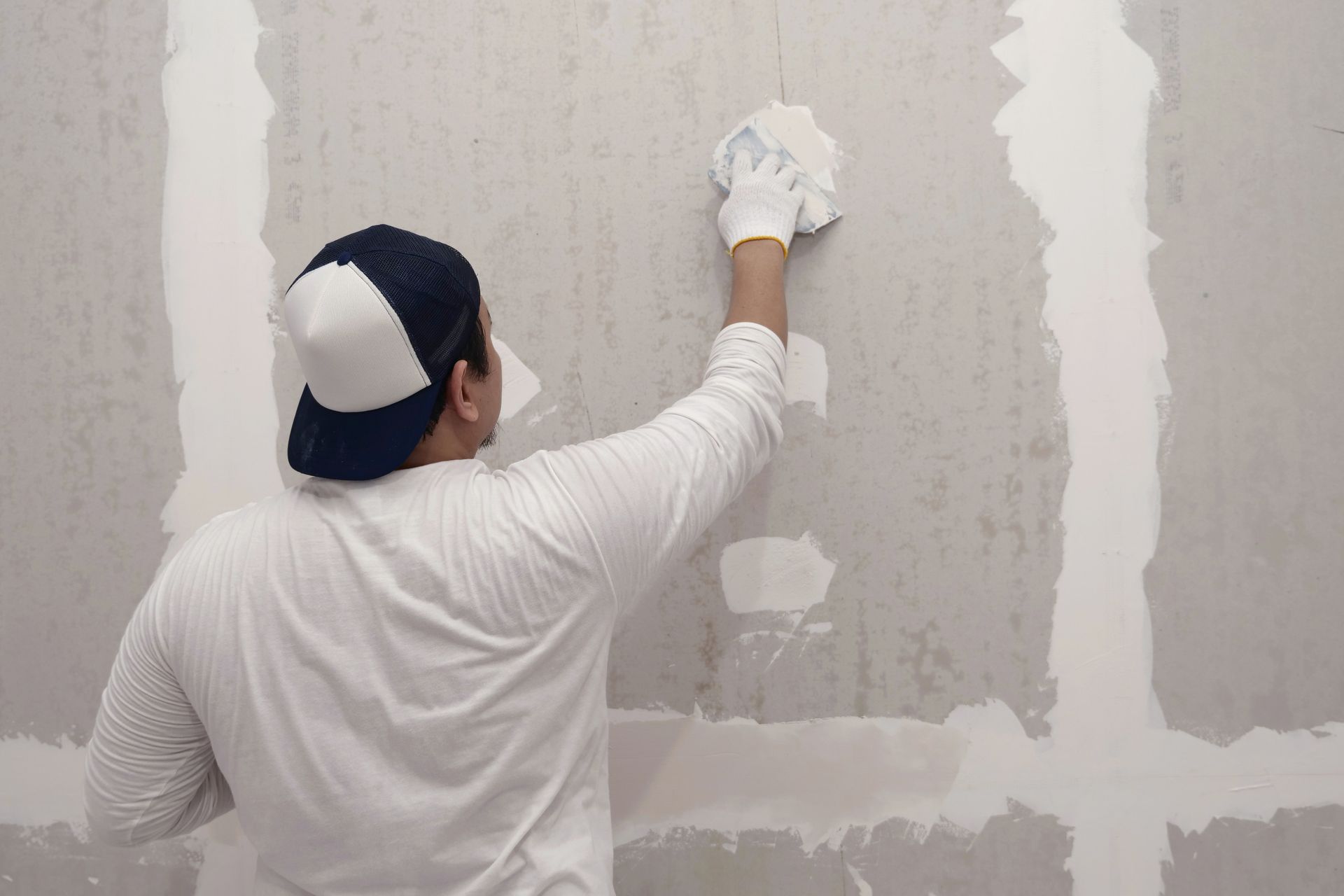 Person in white shirt and cap, applying compound to drywall with a sponge.